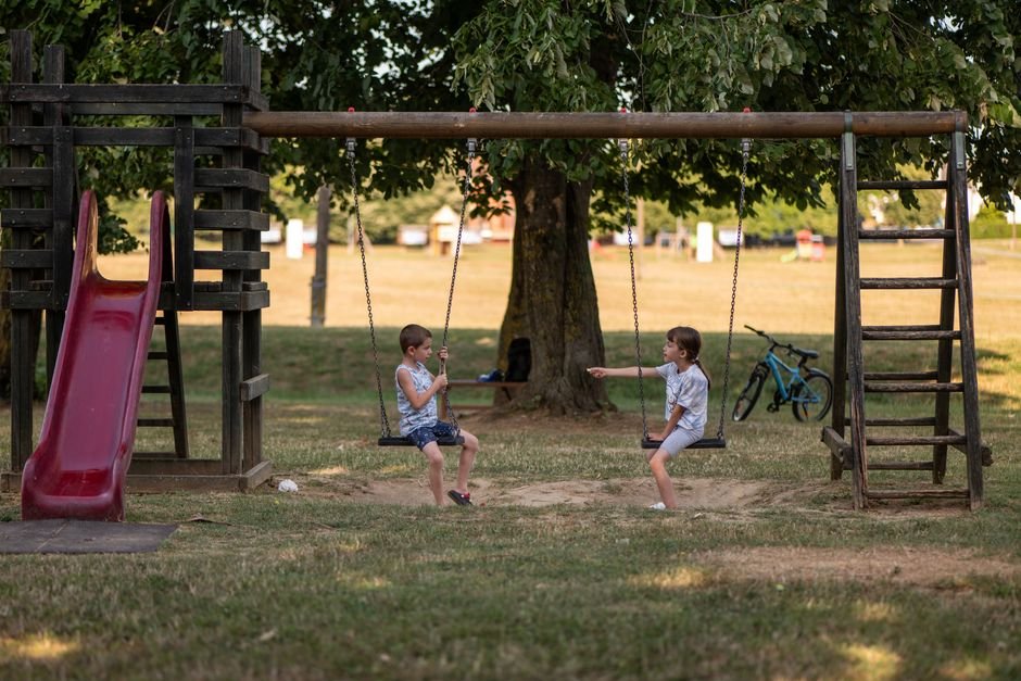Vaikai džiugiai sūpuojasi saulėtame parke, puiki žaidimų aikštelės veikla